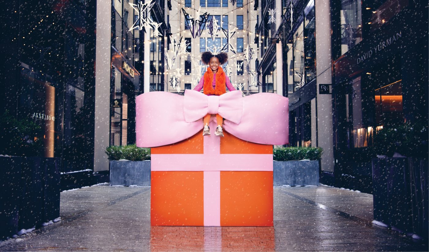 A girl sits on a giant holiday gift.