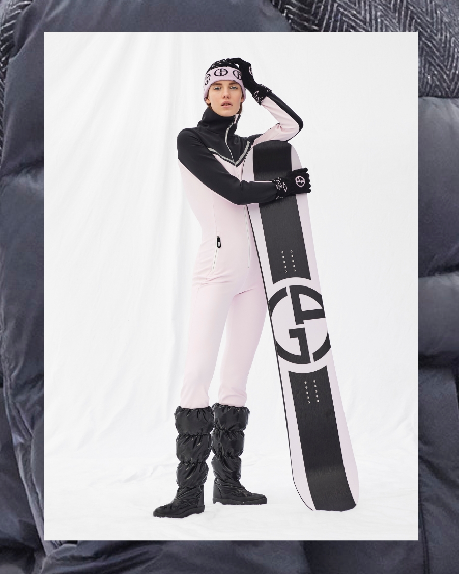 A woman poses with a pink and black Giorgio Armani snowboard and snowsuit from Armani's FW21 Collection