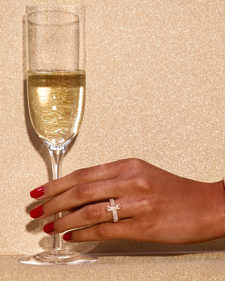 A woman's hand holding a champagne glass and wearing a pink diamond ring.
