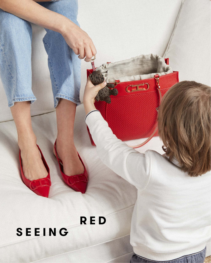 Woman sitting on sofa and child holding on bear figure accessory handed by the woman, red Carolina Herrera shoes and bag