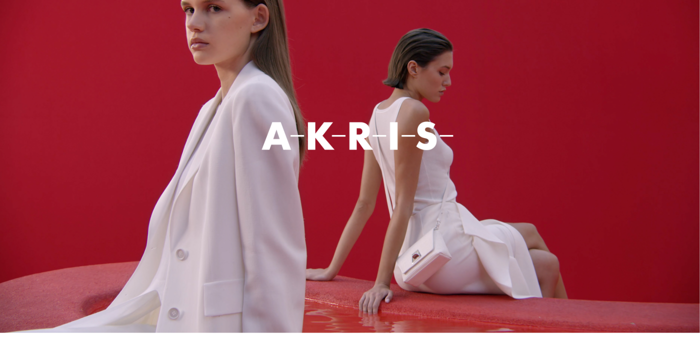 Two women sitting on red sofa - AKRIS logo in the center