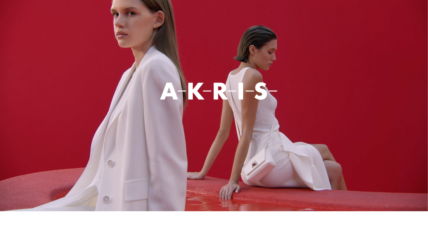 Two women sitting on red sofa - AKRIS logo in the center